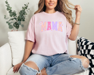 Light pink (blossom) graphic tee with bold font that says mama in uppercase letters.  The fun summer design has bright purple, dark pink, and peach lettering.  Attached to the letters are white daisies.  