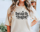 beach shirt made with ivory comfort colors tshirt with black design that says beach babe.  Subtle wave, palm tree, sun, and bird outlines around the words. 