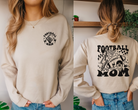 Football mom sweatshirt with design on front and back.  The front is a small upper corner logo that says football mom with a skeleton hand.  The back is big and says football mom with lightnight bolt, checkers, a football, and a melting smiley face with a helmet. The shirt color is sand and the dseign is black.