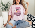 blossom colored (light pink) mom graphic tee with a 90s theme design.  The design says mind your own motherhood in pink, checkered black and white and a yellow melting smiley face.  There are also two small daisies.  